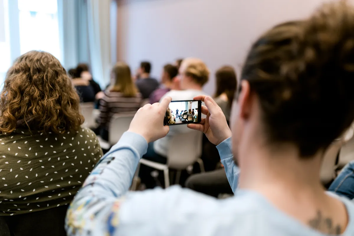 Teilnehmende fotografieren mit dem Smartphone den Workshop-Raum